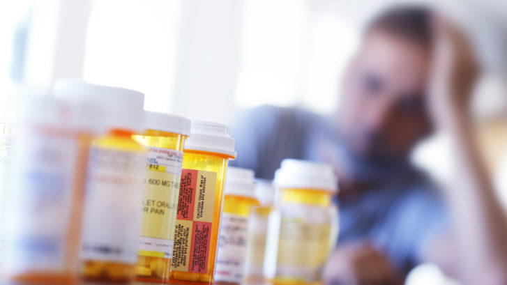 A man looks at a collection of opioid medication with his hand on his head, upset.