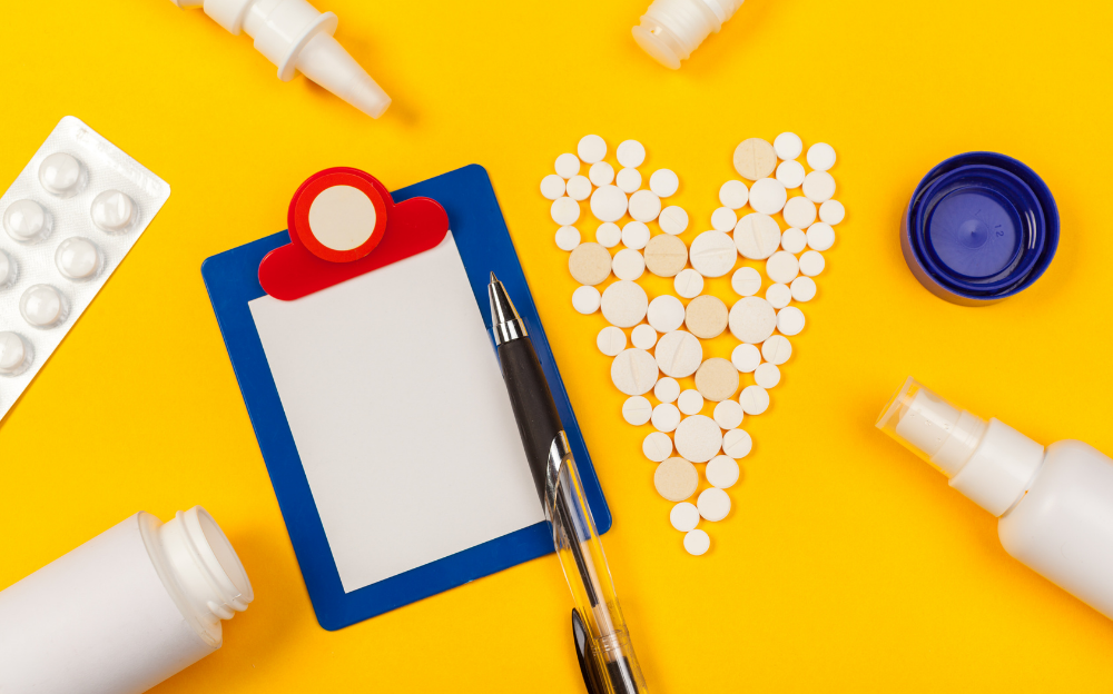 It is an image of a child's clipboard with a sheet of paper and a pen, pills spread out in the shape of a heart, surrounded by white tubes, cannisters, and spray bottles on a sunny yellow background.
