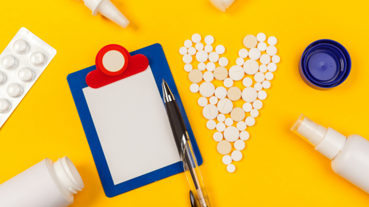 It is an image of a child's clipboard with a sheet of paper and a pen, pills spread out in the shape of a heart, surrounded by white tubes, cannisters, and spray bottles on a sunny yellow background.