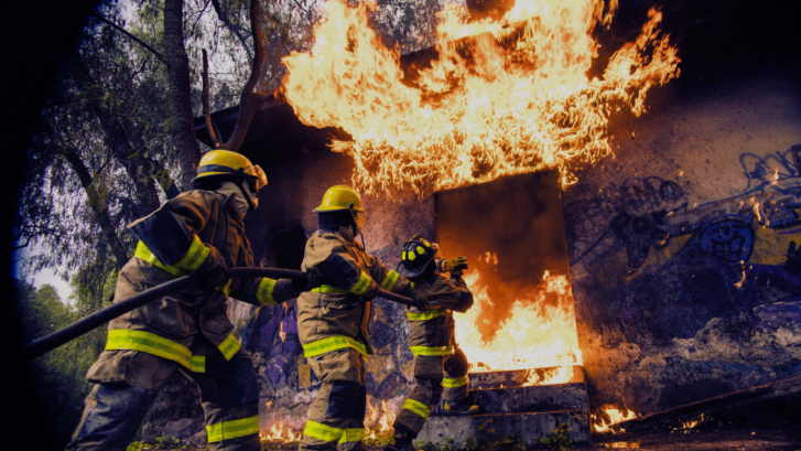 An image of three firemen holding a large hose and directing water into a burning building.