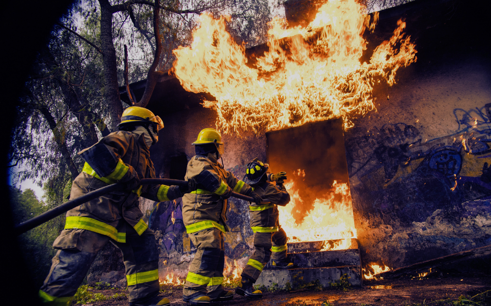 An image of three firemen holding a large hose and directing water into a burning building.